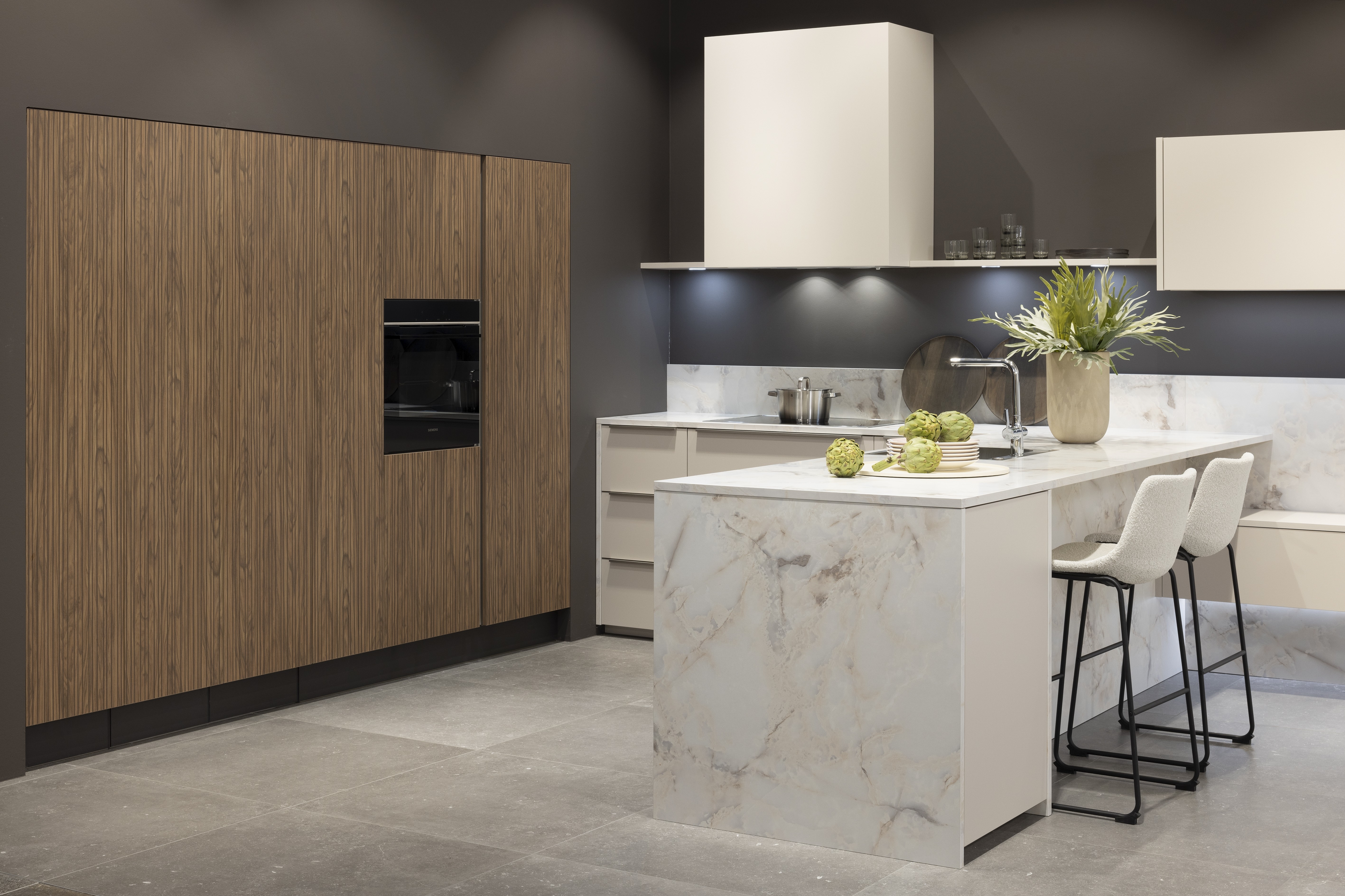 APL: Marmor Bianco 25 mm NB Front: Feel Sahara softmatt Front: WArtline Stripe Wood Choco Korpus: Sahara und Graphit Griff: Kehlleiste Edelstahloptik, und Griffe Edelstahloptik Geräte: Siemens  Armatur: Reginox Spüle: Reginox   Features: eingekoffertes Schrankelement, Tür zum HWR in Frontmaterial, niederer Sockel, Hängeoberschränke asymmetrisch mit Dunstabzug (als Esse geplant), Ecklösung mit LeMans Auszug, Theke mit Essplatz, Ordnungssystem Holz in Auszügen, Downlight in Arbeitsplatzbeleuchtung