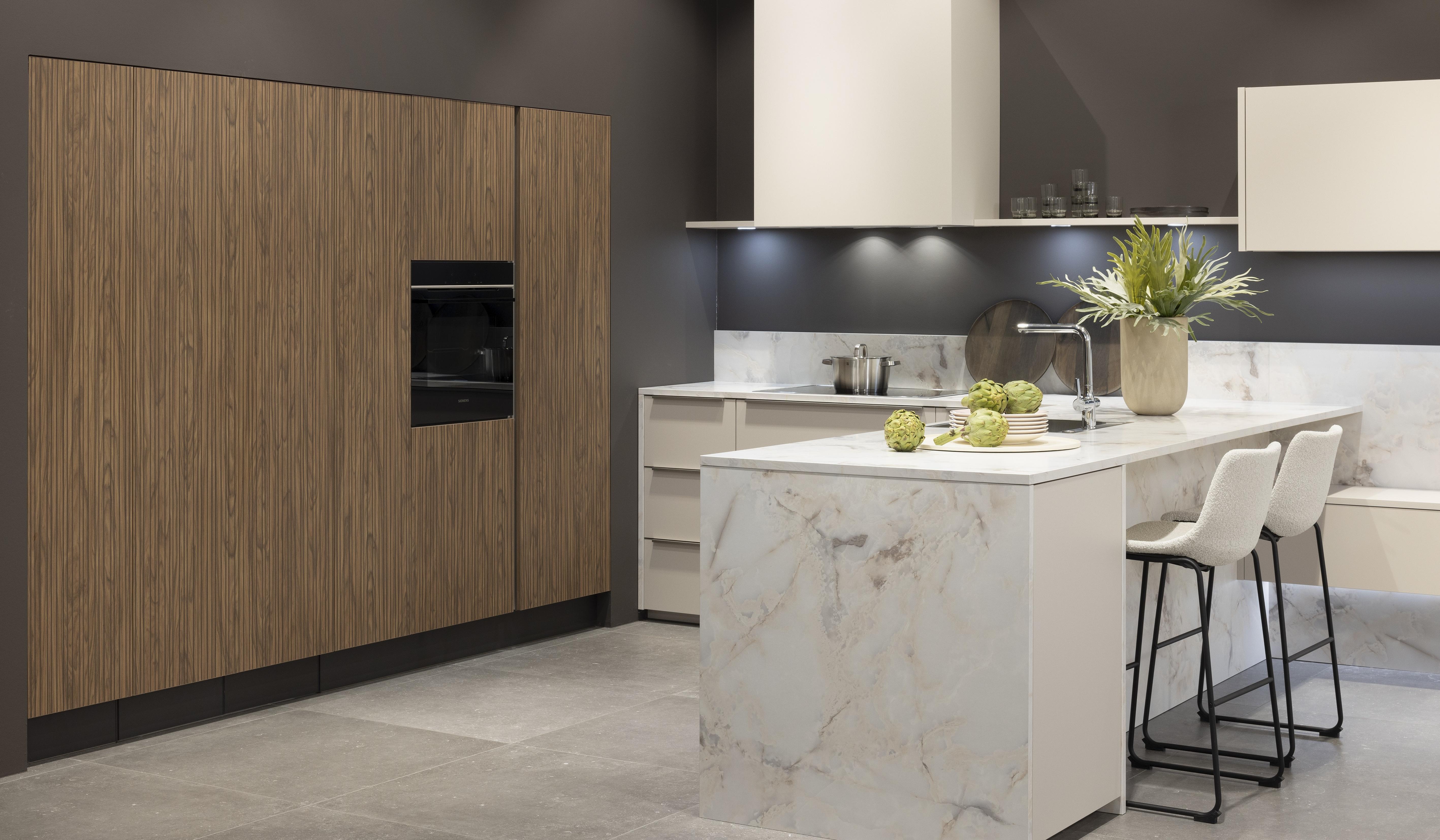 APL: Marmor Bianco 25 mm NB Front: Feel Sahara softmatt Front: WArtline Stripe Wood Choco Korpus: Sahara und Graphit Griff: Kehlleiste Edelstahloptik, und Griffe Edelstahloptik Geräte: Siemens  Armatur: Reginox Spüle: Reginox   Features: eingekoffertes Schrankelement, Tür zum HWR in Frontmaterial, niederer Sockel, Hängeoberschränke asymmetrisch mit Dunstabzug (als Esse geplant), Ecklösung mit LeMans Auszug, Theke mit Essplatz, Ordnungssystem Holz in Auszügen, Downlight in Arbeitsplatzbeleuchtung 